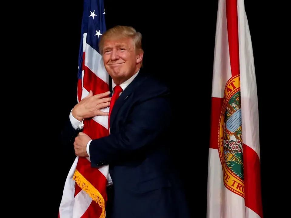 File photo of Donald Trump hugging an American flag on a dark stage.